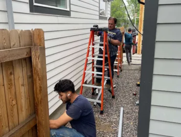 Electricians working on power lines beside house